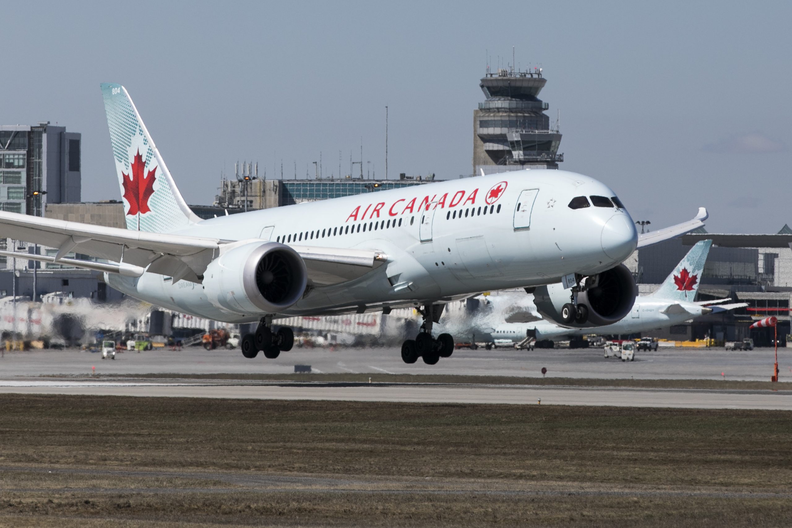 An Air Canada airliner sits on the tarmac with a bright red maple leaf emblazoned on its tail.