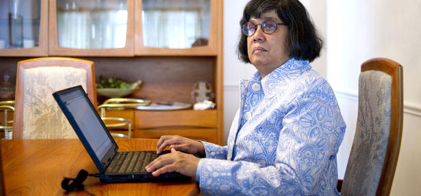 Donna Jodhan, a woman with short dark hair and glasses, sits at a table with a laptop in front of her.