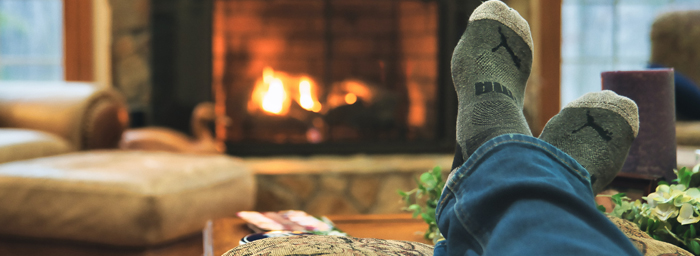 A photo of someone's socked feet propped up on a coffee table in front of a cozy fire in a fireplace.