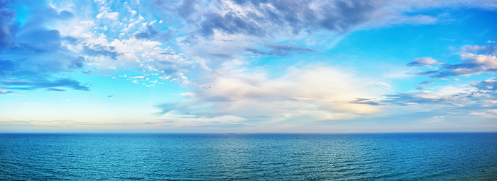 A photo of the boundless sea at daytime, with no land anywhere on the horizon but a few clouds in the sky.
