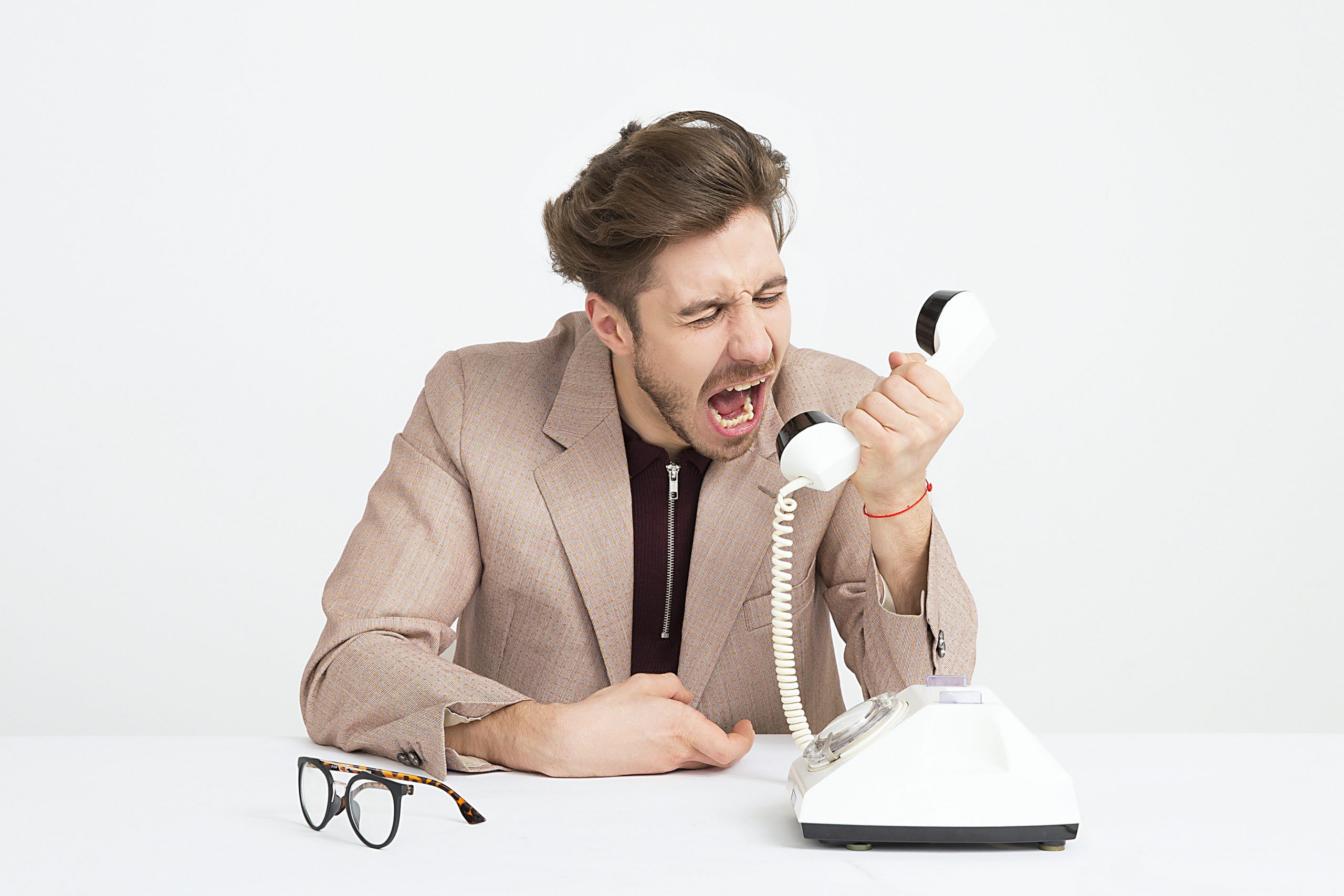 A photo of a white man with brown hair and glasses yelling exasperatedly into a phone.