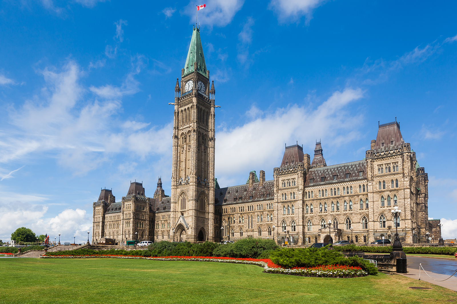 A photo of the center block of buildings at Parliament Hill in Ottawa, Canada, at midday under a clear blue sky with white clouds.