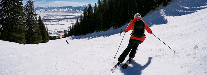 A skier slaloms down a mountain covered in fresh snow under a bright winter sun.