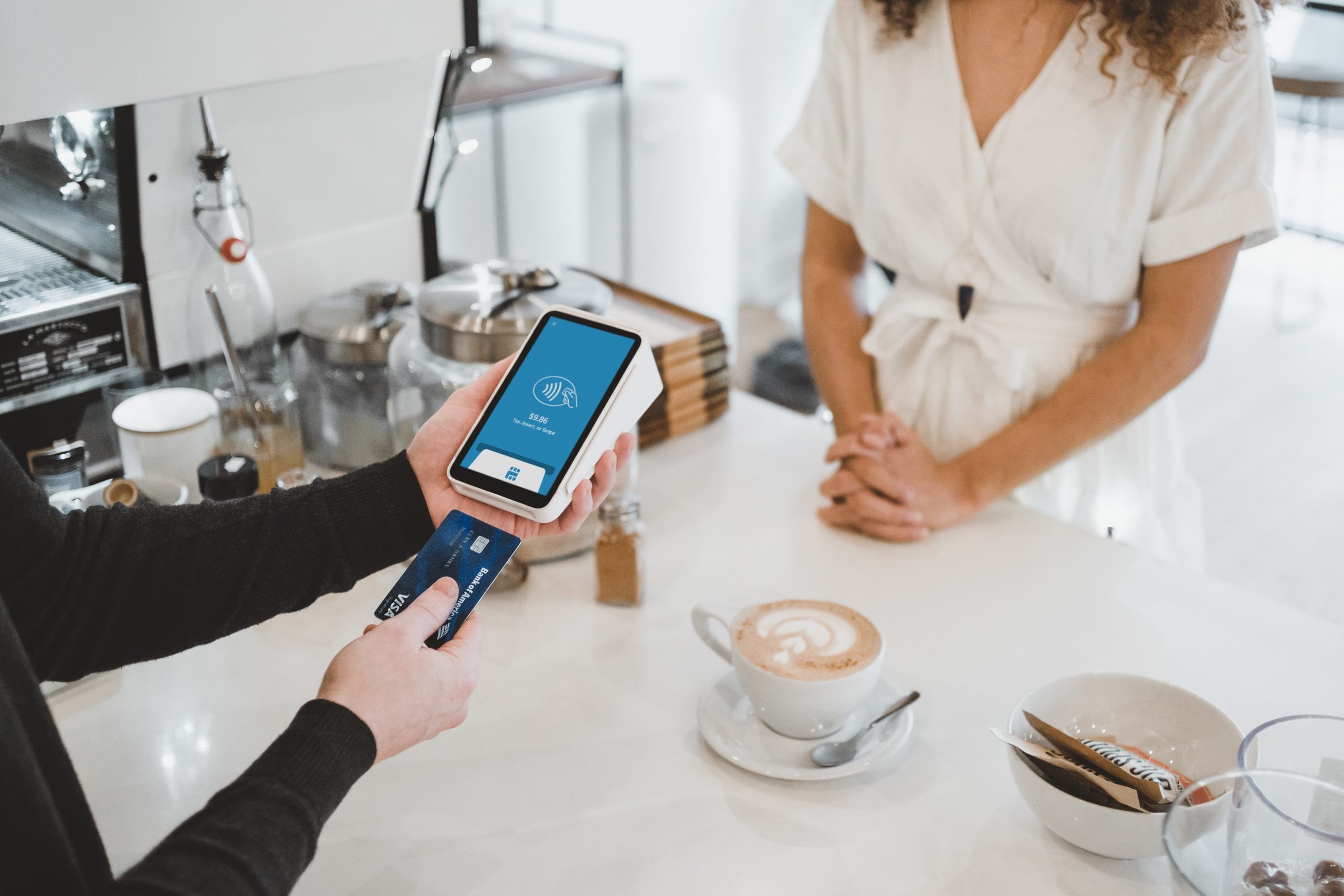 A customer pays for coffee in a café using a portable credit/debit machine with a touchscreen.