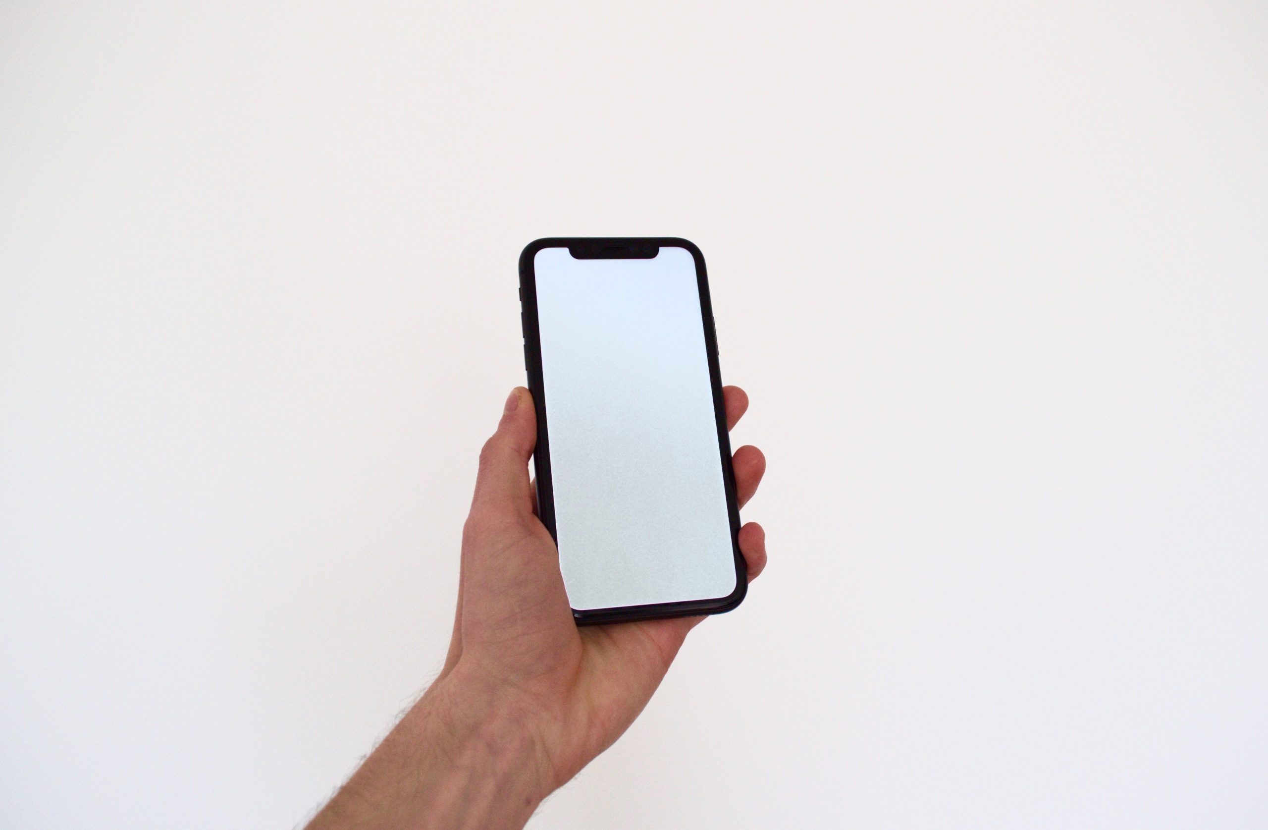 A man holds out his phone to the camera, as if to show something on the screen, but the screen is a white blank.