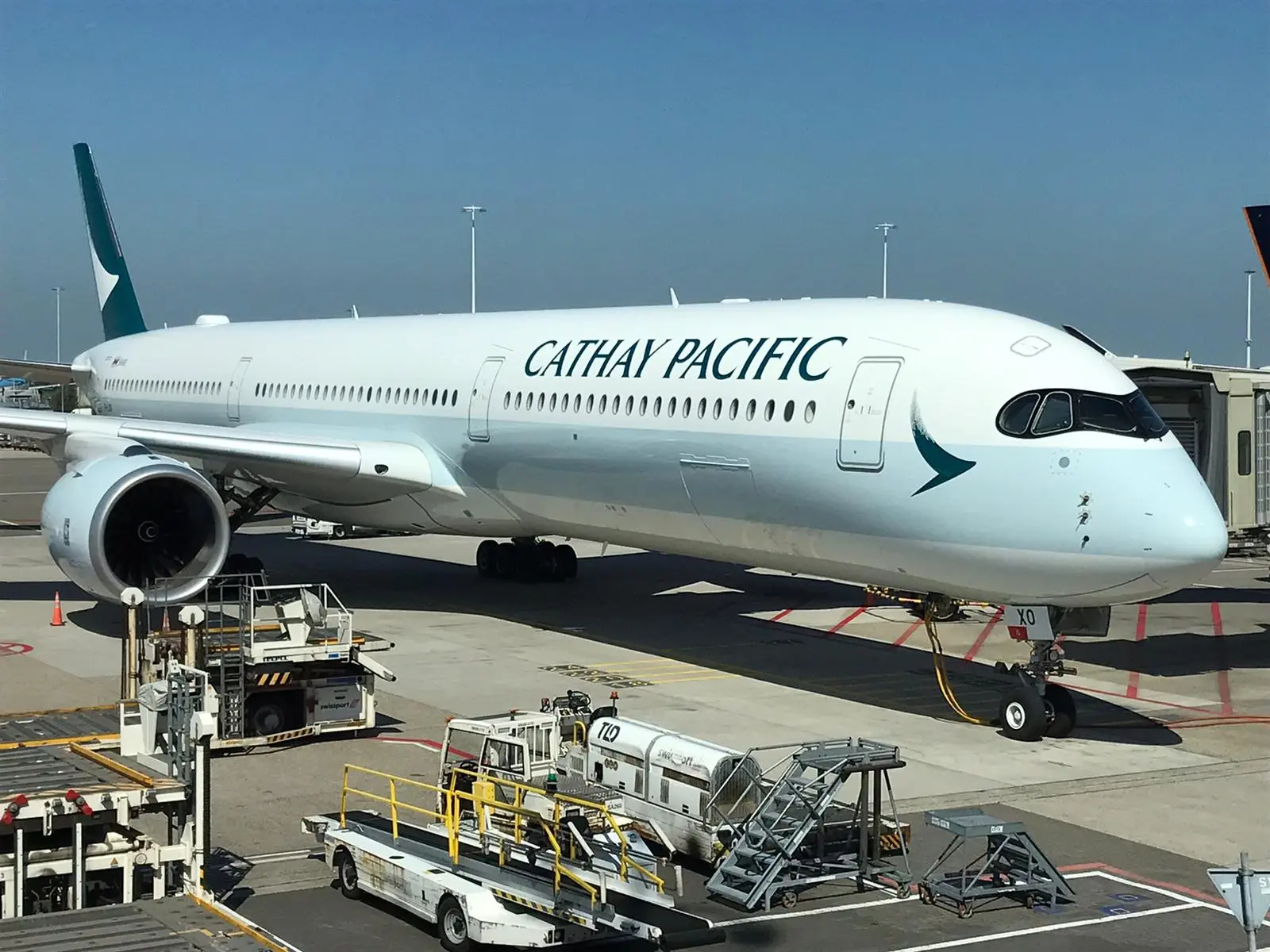 A Cathay Pacific airplane sitting on the tarmac, being loaded with luggage.