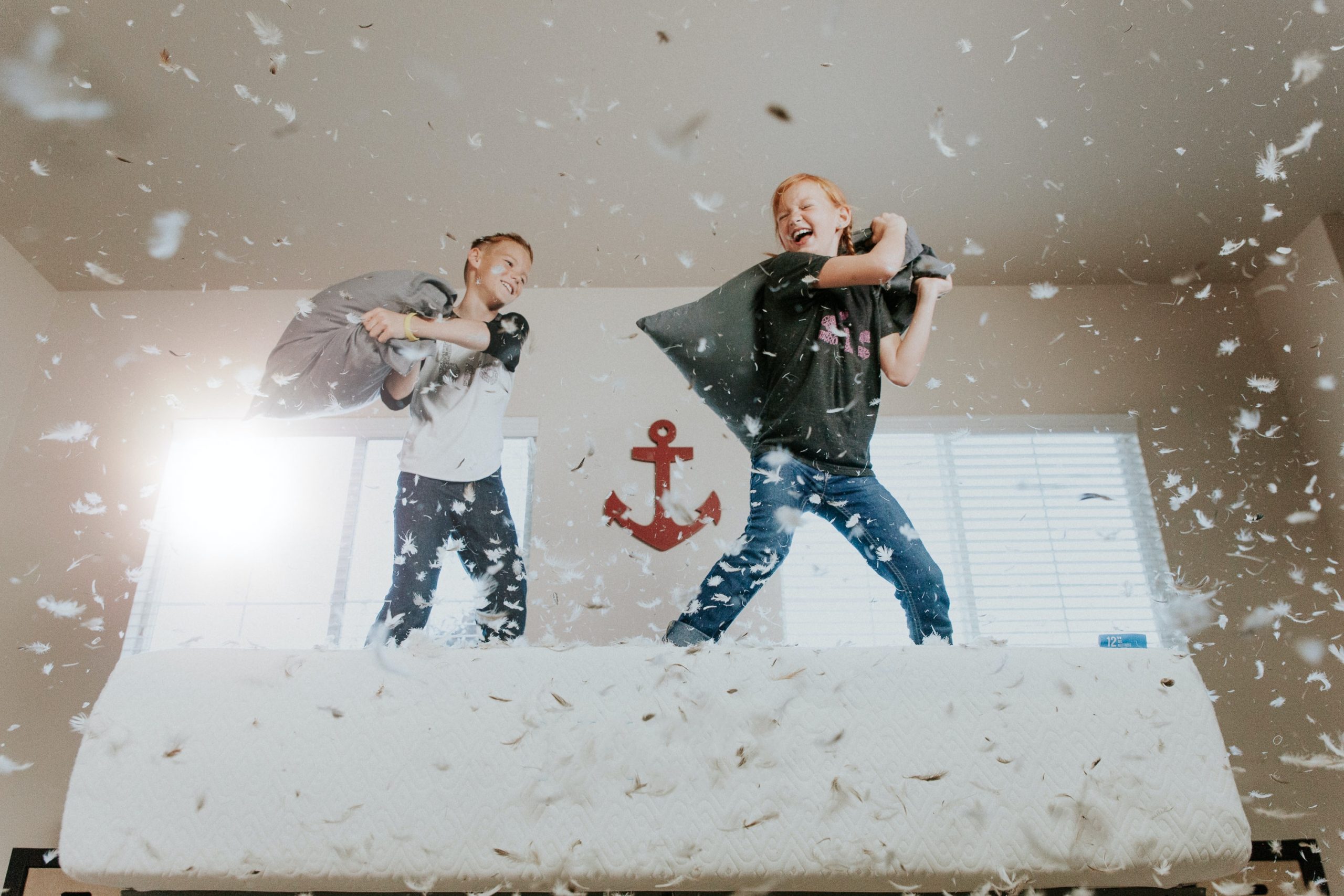 A pair of boys having a pillow fight on a bed, laughing as down feathers explode everywhere.