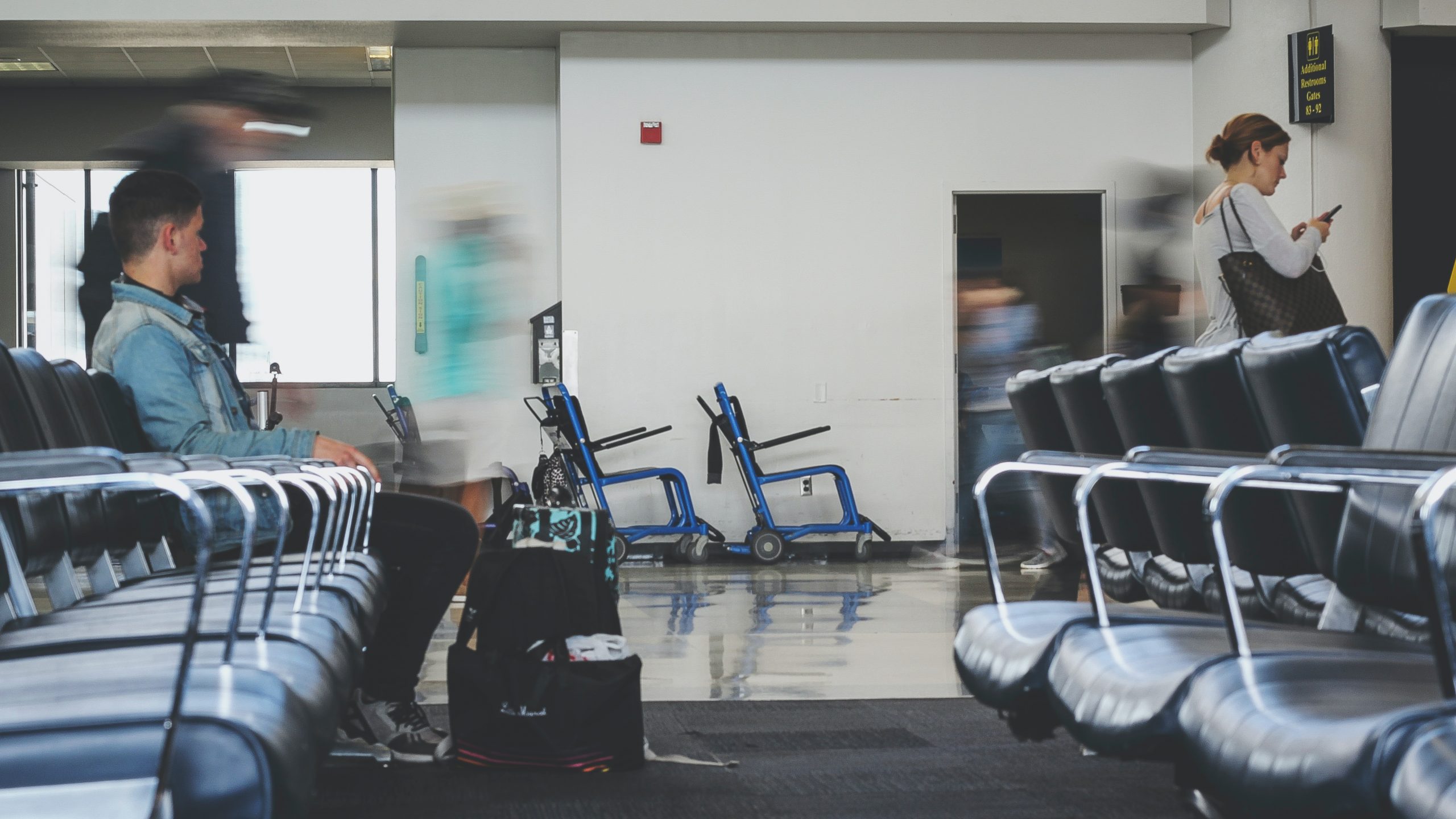 A photo of blurry people walking by two abandoned airport wheelchairs.