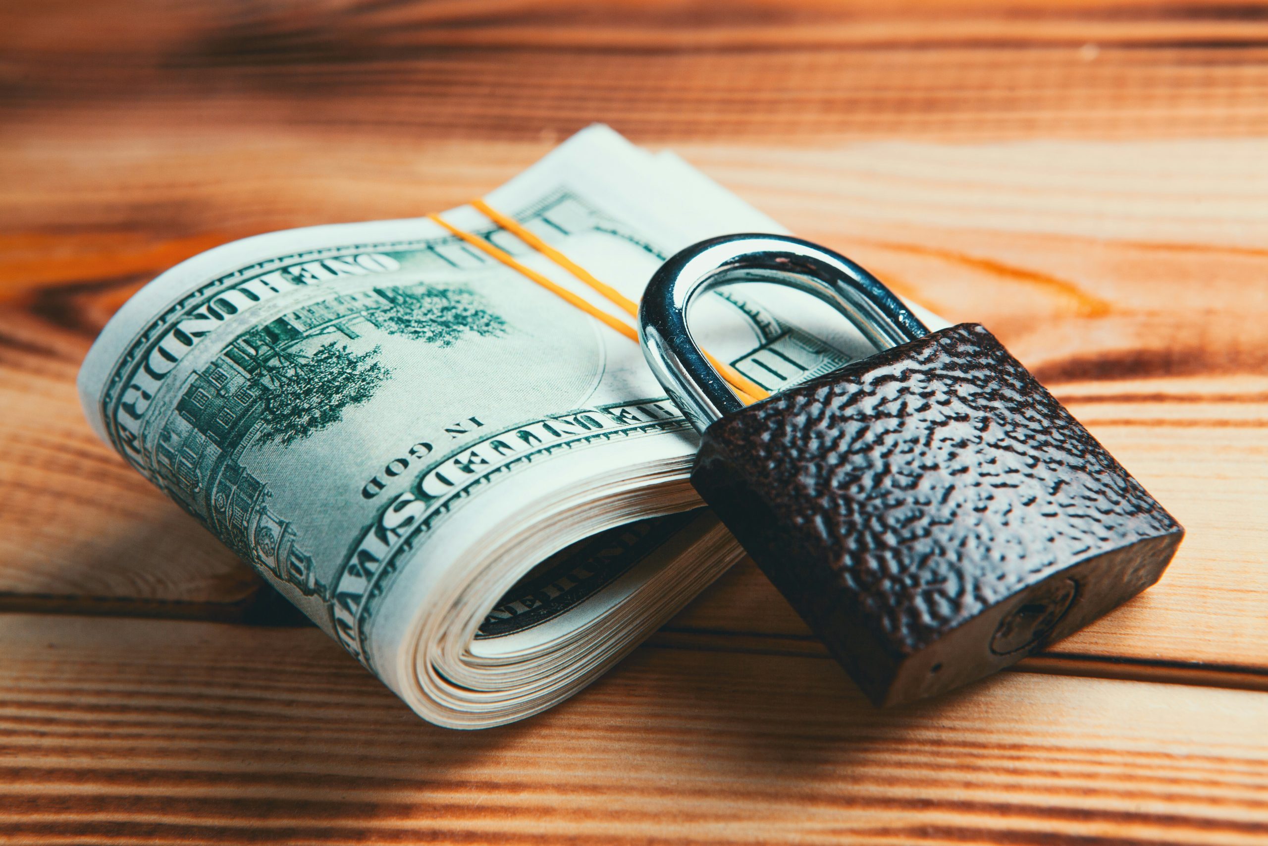 A folded stack of $20 bills sits underneath an iron padlock.