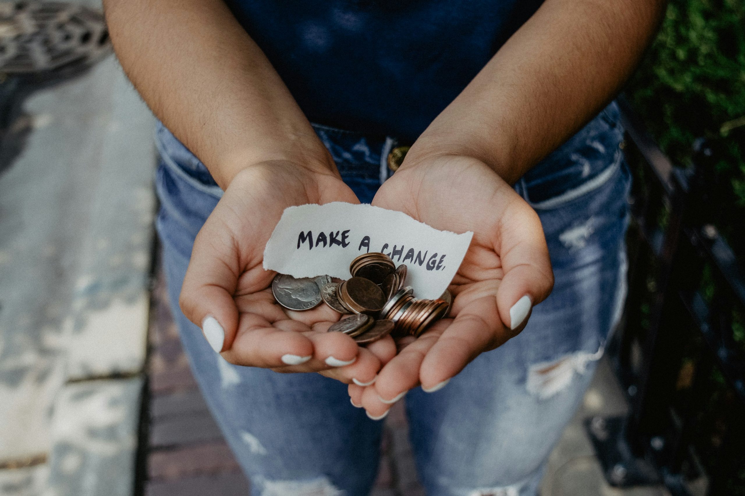 A photo of a woman's outstretched hands, in which she holds some small change and a sign saying, "Make a change."