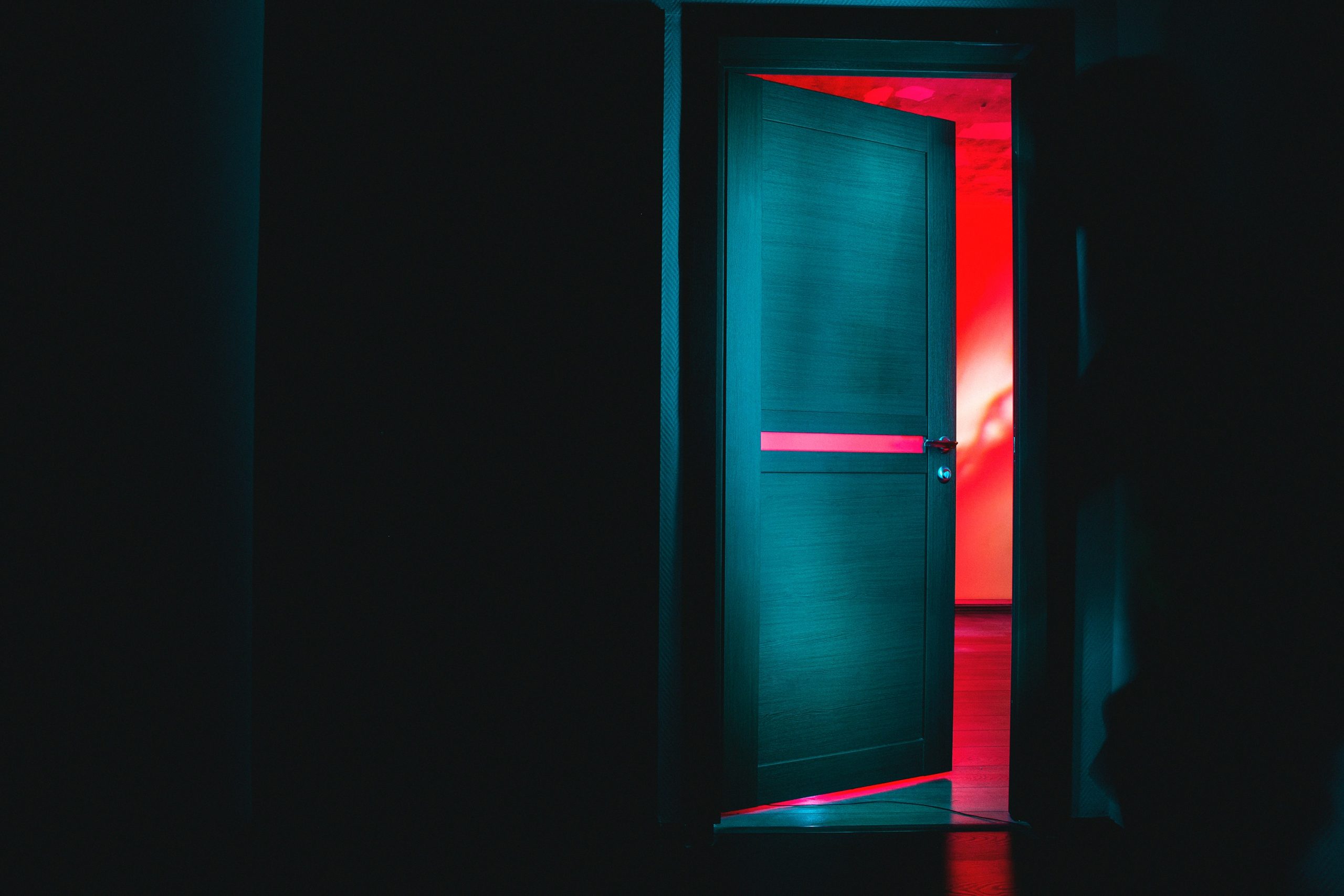 A photo of a dark doorway with the door half-open, beyond which are bright colours.