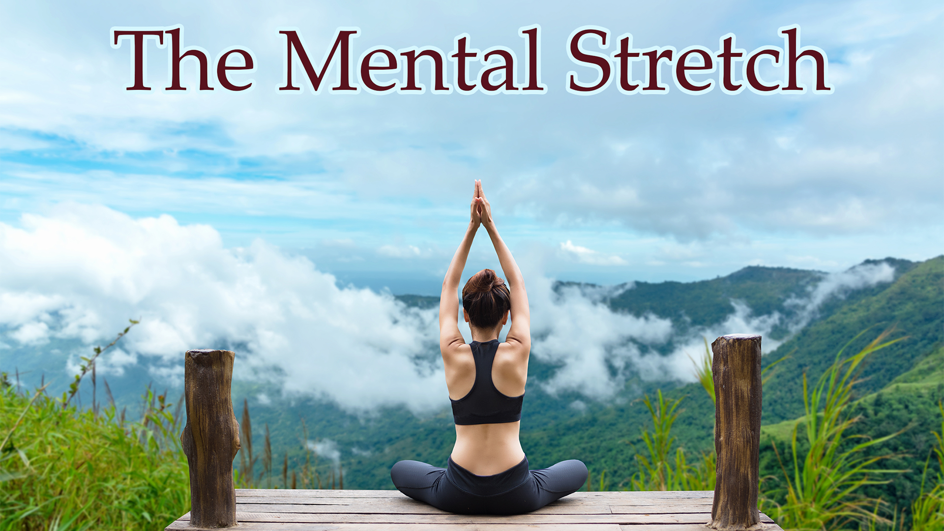 A woman is seated cross-legged on a wooden platform facing a lush, mountainous landscape with low-hanging clouds and a blue sky. She wears a black sports bra and leggings, and her arms are raised overhead with palms pressed together in a yoga pose, emphasizing mindfulness and calm. The scene is framed by grass and two wooden posts, with the text 'The Mental Stretch' in large, elegant red font centered at the top, evoking a theme of mental clarity and inner peace through nature and meditation.